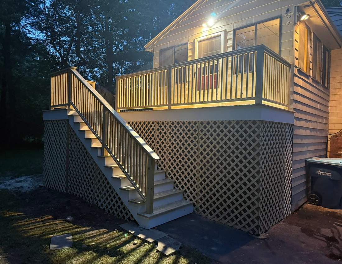 Elevated pressure-treated wood deck with stairs, railings, and lattice skirting lit at dusk on a South Shore home